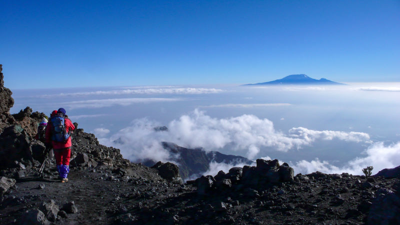 Climbers hike down from the summit of Mount Meru in Arusha National Park in Tanzania with Kilimanjaro in distance