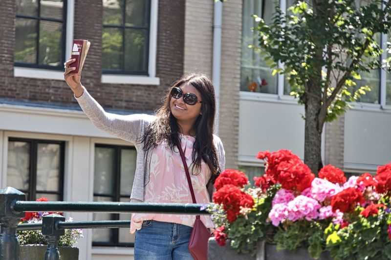 Young Indian woman taking a selfie by flowers, street scene, happy
