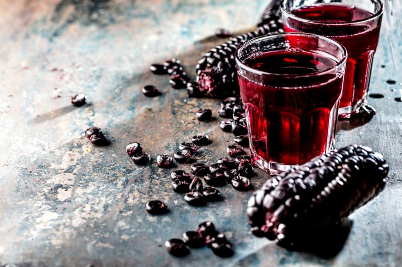 Two glasses of chicha morada, or Peruvian purple corn drink, non-alcoholic, on a table with pruple corn cob next to them