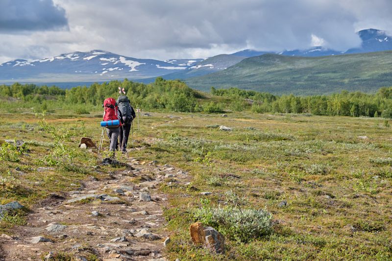 Two trekkers with rucksacks in green landscape among mountains