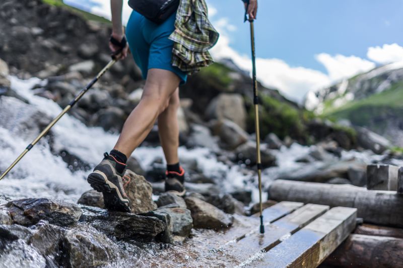 Ours. S. Woman trekker walking in mountains across stream using trekking poles