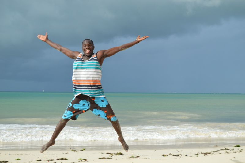 Man in beach clothes jumping for joy on beach in Kenya