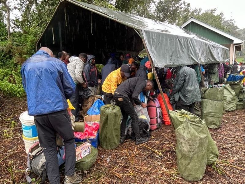 Porters under a tent in rainy weather getting ready for a Kilimanjaro climb