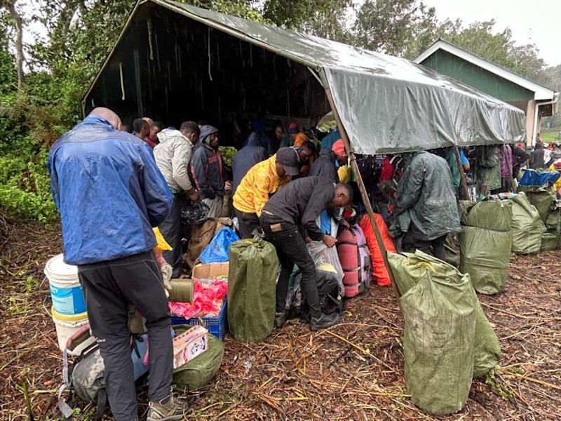 Porters under a tent in rainy weather getting ready for a Kilimanjaro climb