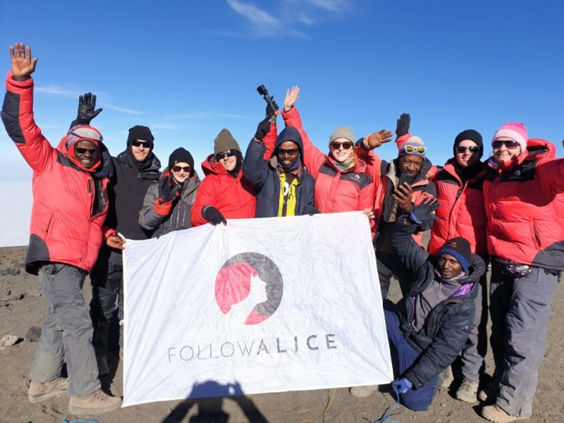 Group photo with Follow Alice sign at top of Kilimanjaro