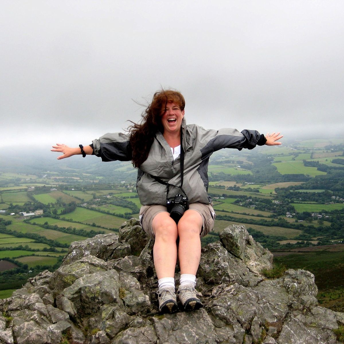 Happy smiling woman sitting on rock farms wind