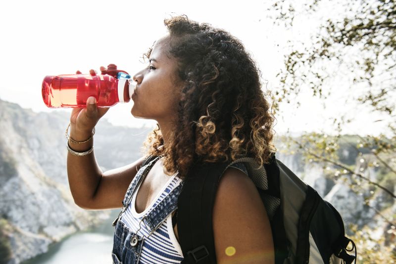 Black female backpacker:hiker woman drinking water out of a bottle with lake in background