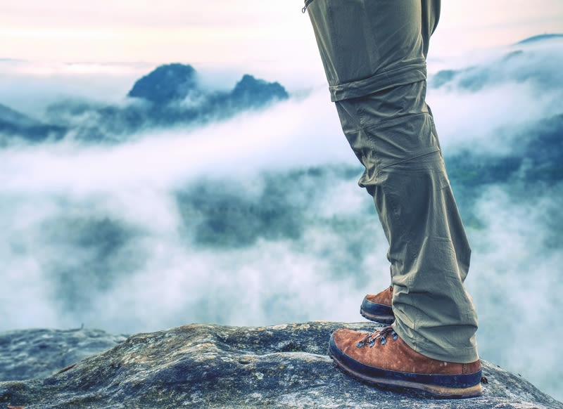 Hiker legs in light outdoor zip-off trousers and comfortable leather trekking boots on rocky peak