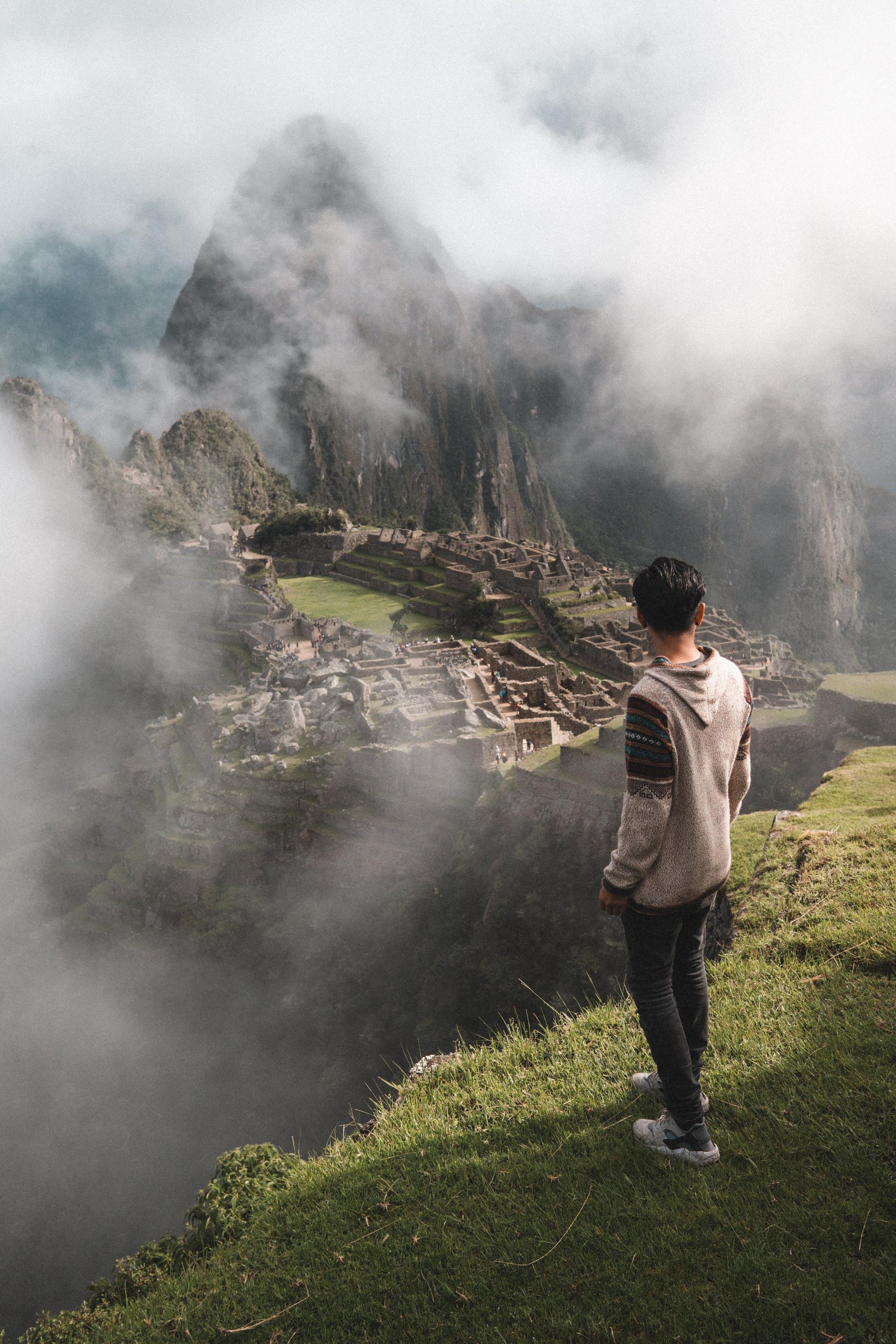 Young man looking down over a misty Machu Picchu, Cusco, Peru