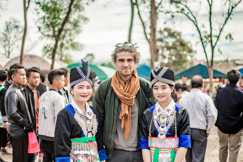 Young man standing with two Hmong women in traditional dress, tourist