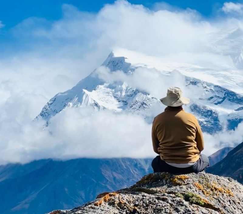 Trekker sitting on rock looking at mountains on Annapurna Circuit