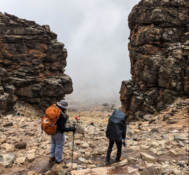 Two climbers with backpacks and rain cover and trekking poles descending to Barranco Camp on Kilimanjaro hike in the mist