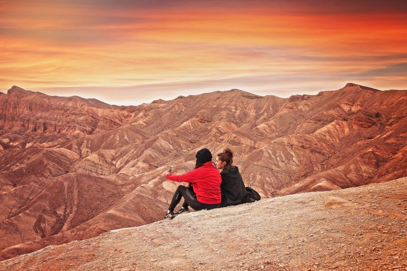 Two female hikers seated in barren, mountainous country