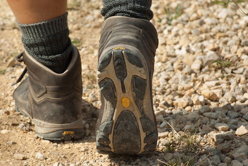 Woman walking along a dirt path in brown, worn hiking boots and long grey socks