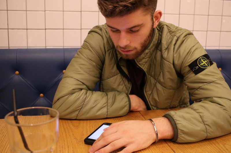 Young man at table looking at cellphone with empty glass in foreground
