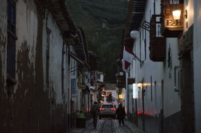 Quiet Cusco city street at dusk with two walkers and a car