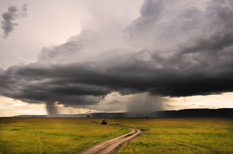 Lone safari vehicle driving on open plain with rain and thunderstorm in distance