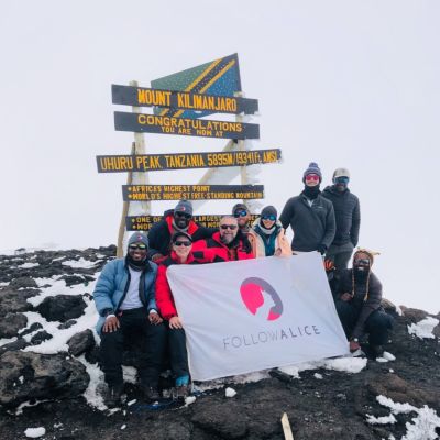 Group of trekkers with Follow Alice flag at Uhuru Peak on Kilimanjaro