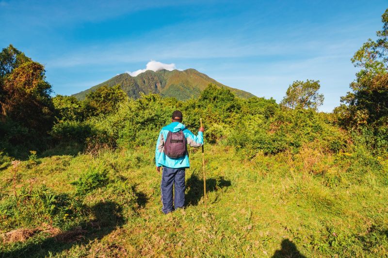 A hiker wearing all weather clothes and a backpack against a Mountain background at Mgahinga Gorilla National Park, Uganda