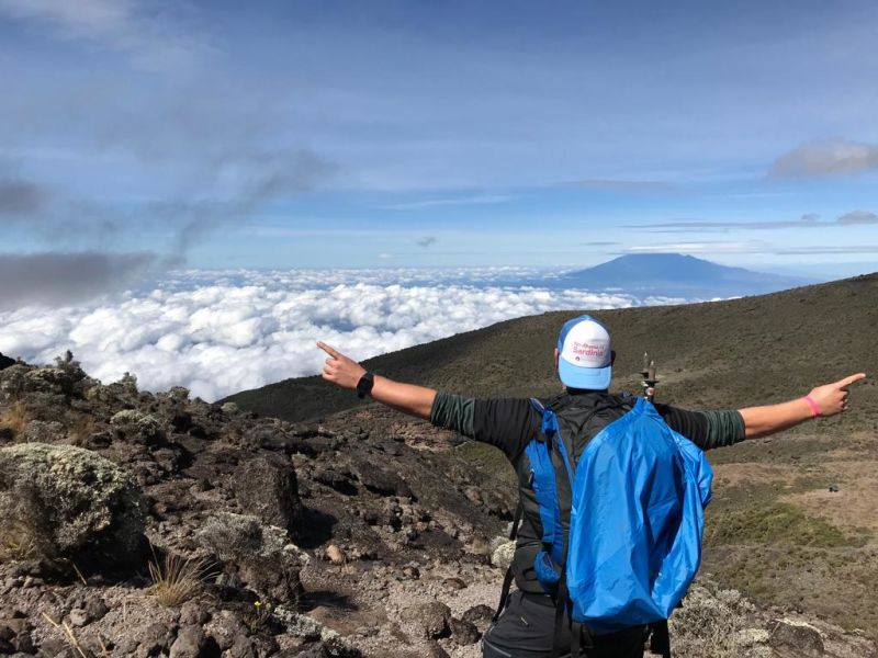 Man in cap looking over cloud bank high on Mt Kilimanjaro