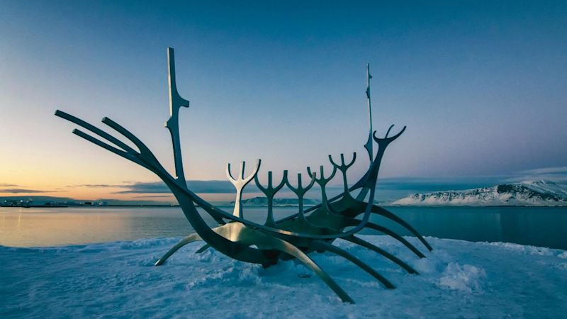 A modernist steel sculpture of the hull of a Viking ship stationed beside a fjord and surrounded by snow