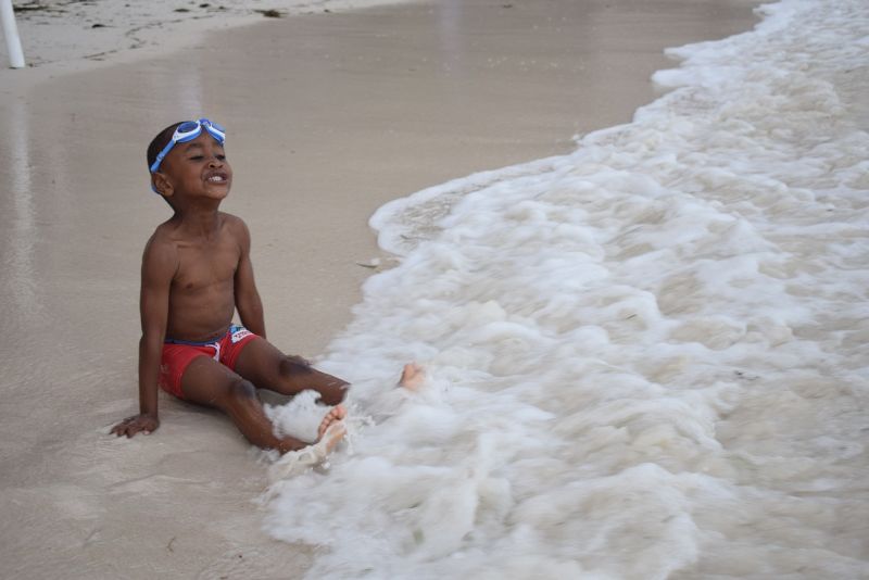 Small boy with goggles on head sitting at the edge of the sea in Kenya