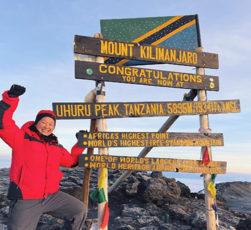 Woman standing on summit of Kilimanjaro by Uhuru Peak sign, August 2022