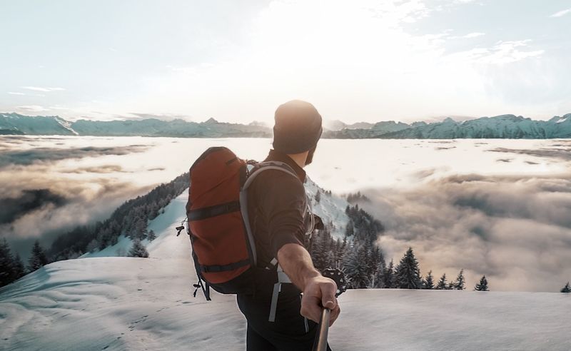 Man with backpack in snowy landscape talking selfie while looking away