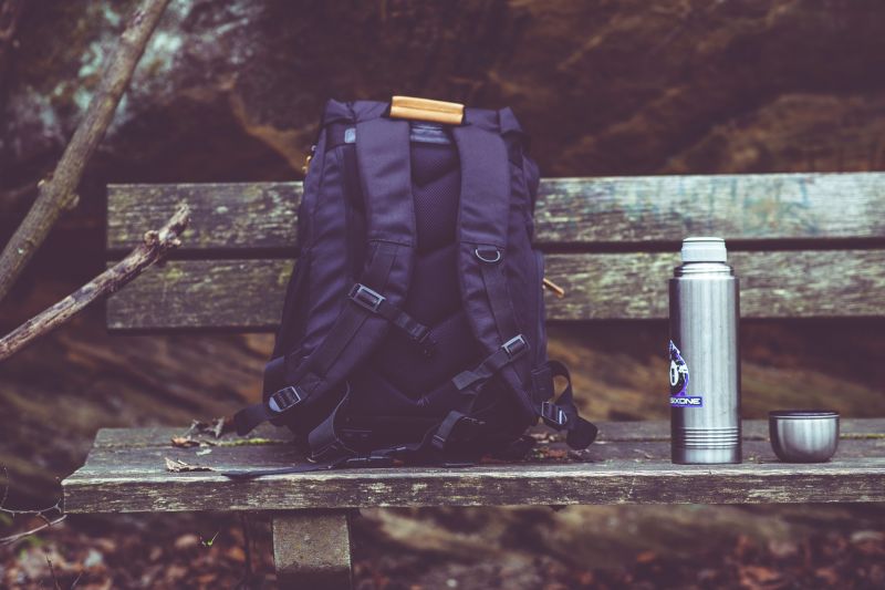 Navy backpack sitting on a bench with a metal flask next to it