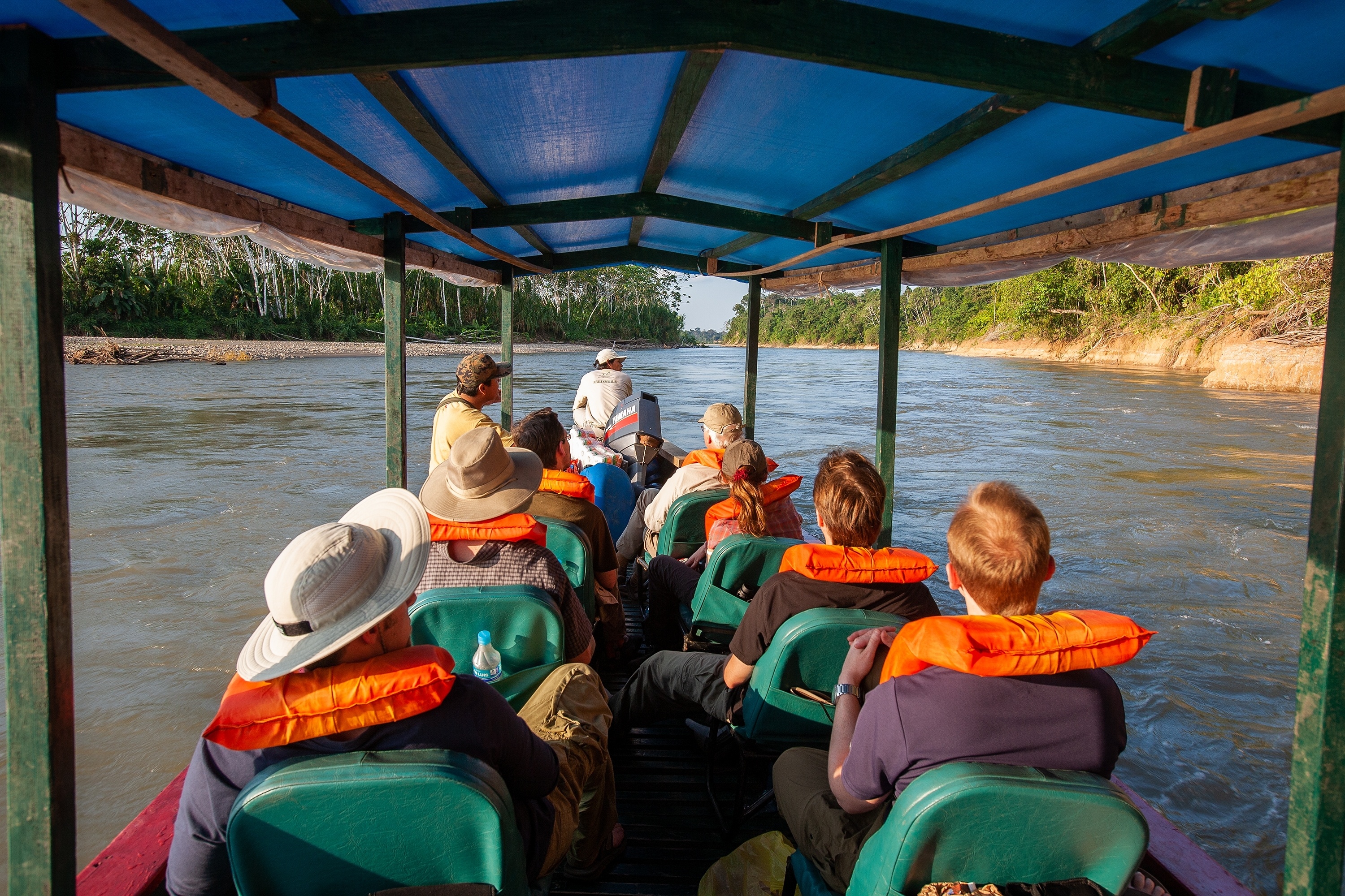 Boat full of people wearing red life jackets on Tambopata River heading to lodge in Peruvian Amazon rainforest/jungle