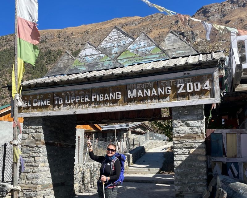 Woman standing beneath sign for Upper Pisang village on the Annapurna Circuit