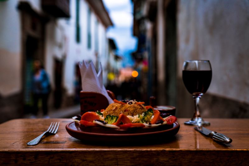 Vegetarian food (quinoa, broccoli, carrot, tomato) served on Italian restaurant terrace with glass of wine, Cusco, Peru