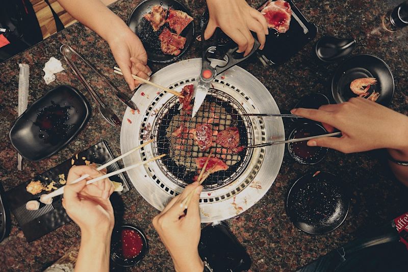 Hands eating food from a shared grill