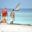 Three local Muslim women walking along beach on Zanzibar with dhow in distance on water