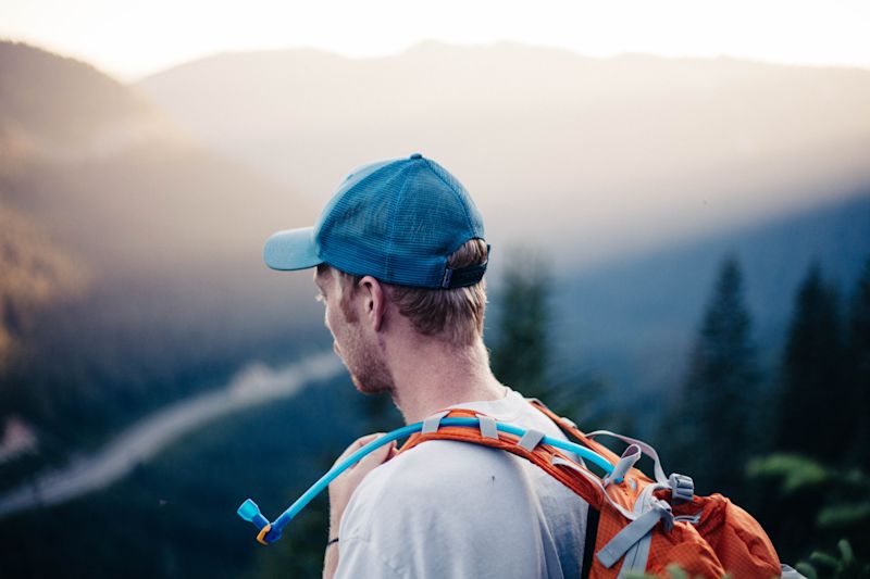 Man in blue cap wearing an orange backpack with a blue hydration hose visible