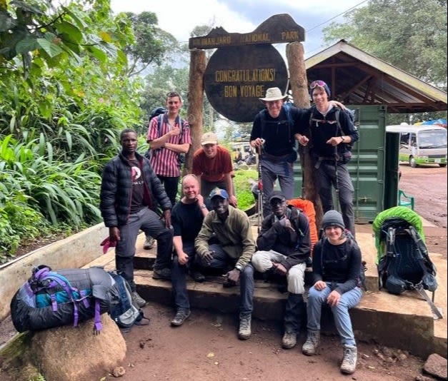 Group picture by the Bon Voyage sign at Mweka Gate on Kilimanjaro
