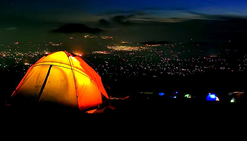 Kilimanjaro campsite at night with tents lit up from inside and a view of the town lights far below and Mt Meru in the far distance