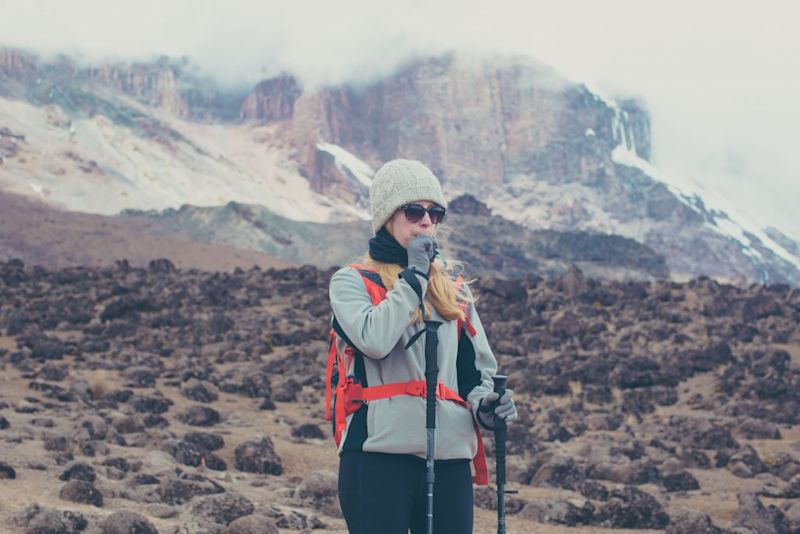 Lady surrounded by mountains stopping to drink some water on her trek