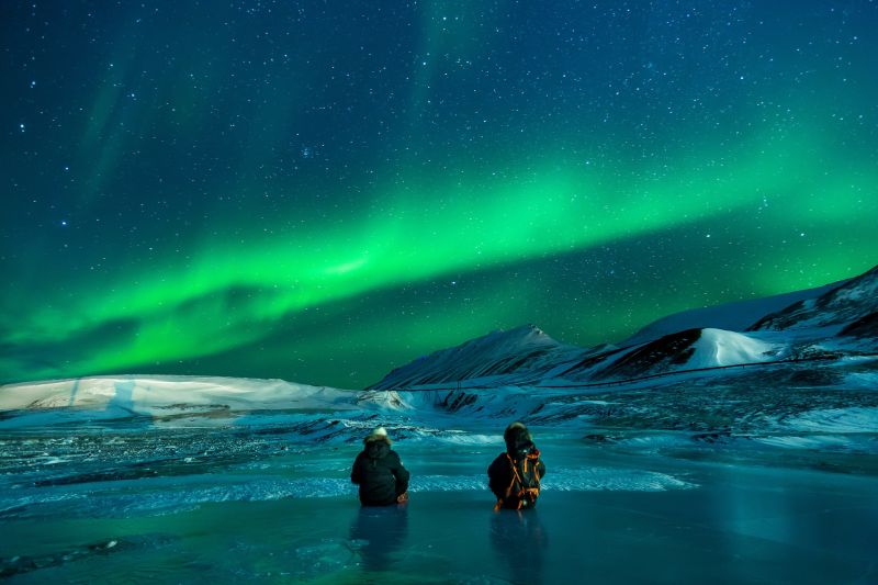 Two adults on ice under aurora borealis