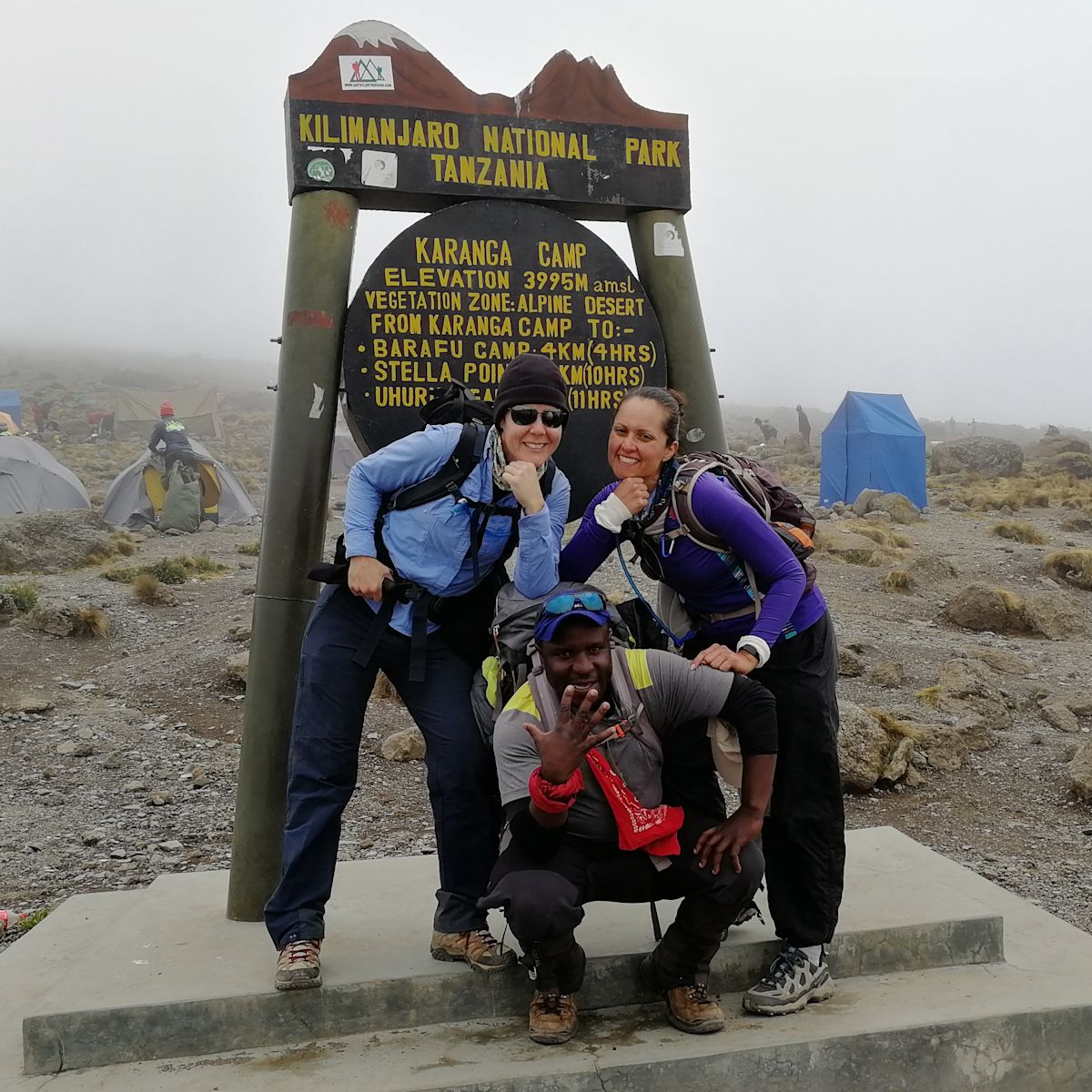 Smiling trio at camp sign on Kili