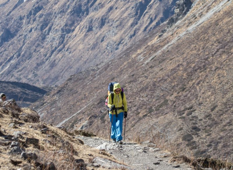 Male trekker hiking in alpine section of Annapurna Mountains with trekking poles and sunglasses on
