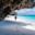 Woman walking under rocky overhang on white-sand beach next to turquoise water in Zanzibar, Tanzania