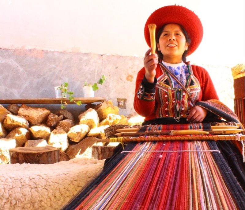 Woman in red hat doing traditional weaving in village of Chinchero, Sacred Valley, Cusco region, Peru