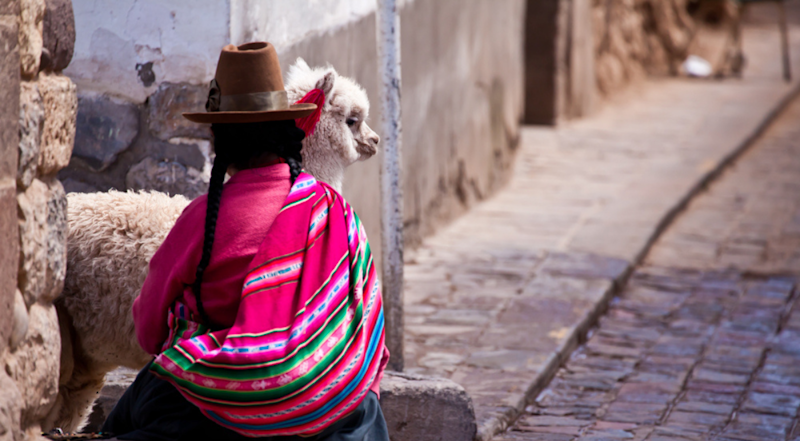 Woman in traditional clothes with alpaca sitting on stone in Cusco - Peru