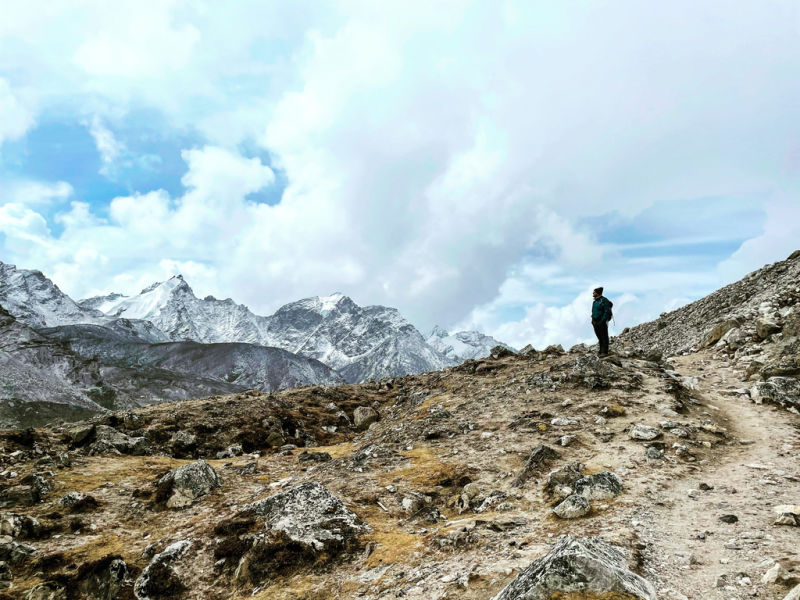 Lone trekker seen from a distance on EBC trek trail high up in barren landscape looking towards snow-capped Himalayan peaks, Nepal (1)
