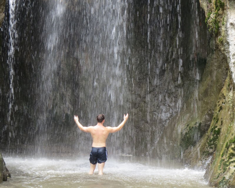 Man in swimming trunks standing under waterfall at Ngare Sero