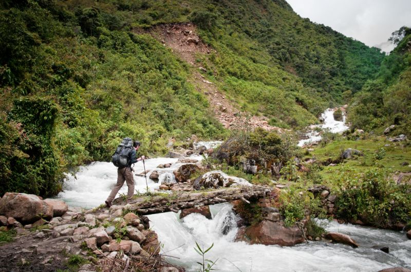 Male trekker with poles crossing river on footbridge on Salkantay Trek to Machu Picchu in Peru