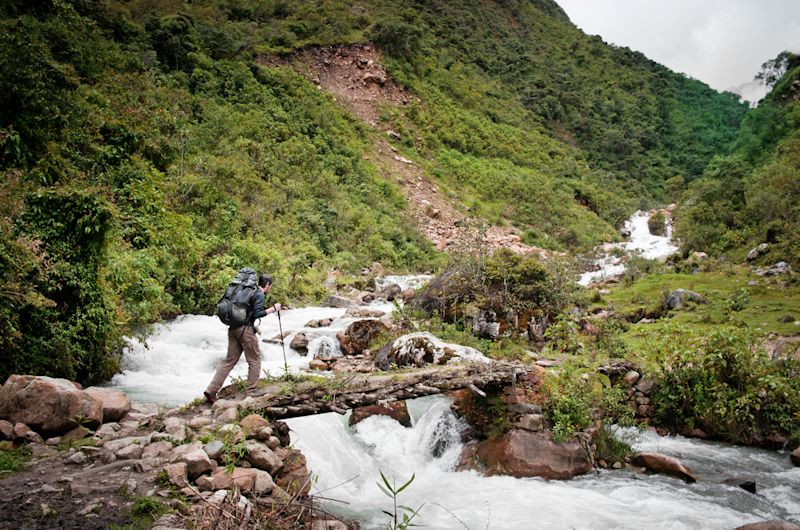 Male trekker with poles crossing river on footbridge on Salkantay Trek to Machu Picchu in Peru