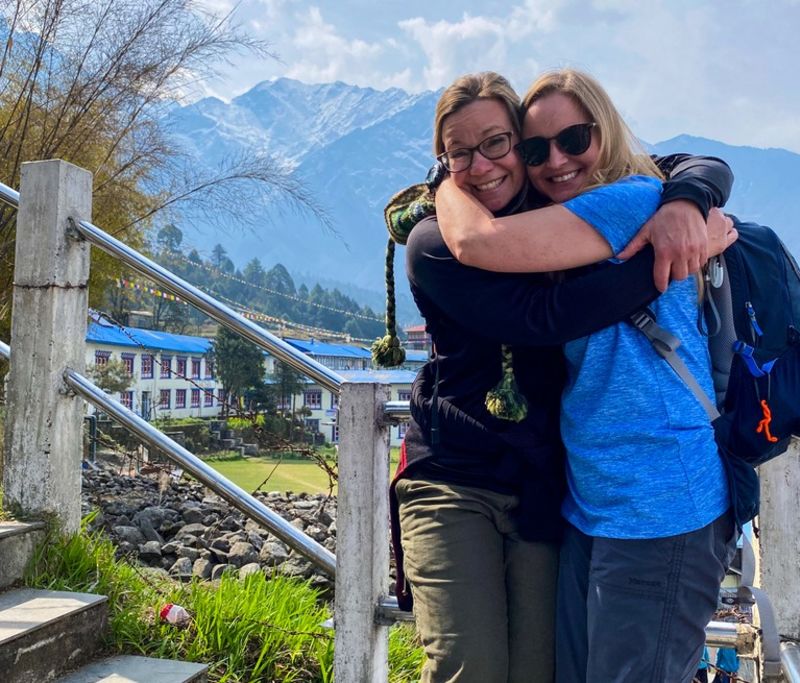 Smiling and hugging woman friends on sunny day on EBC trek, early on, Nepal 