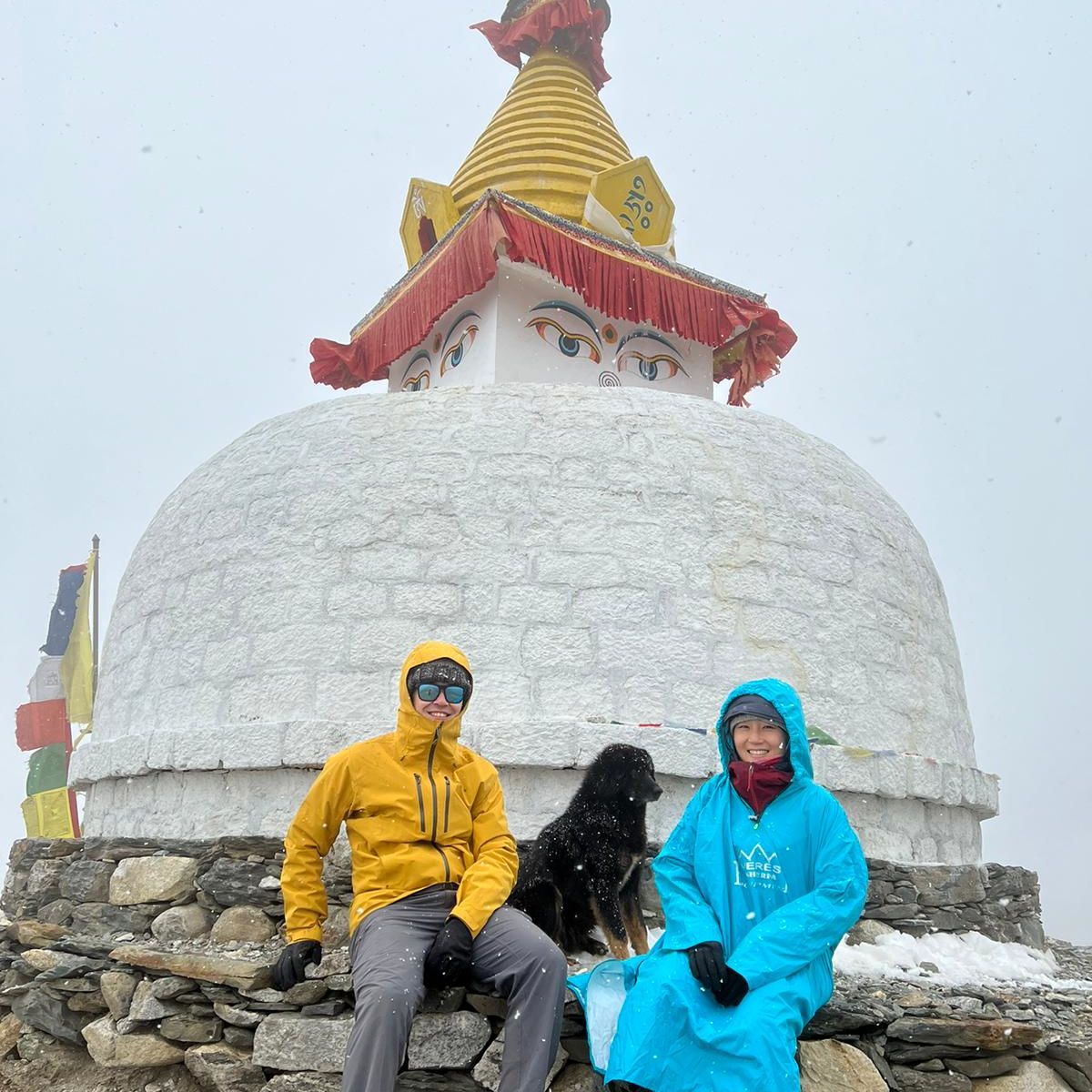 Nepal EBC trek, trekkers sitting with dog by stupa in mist